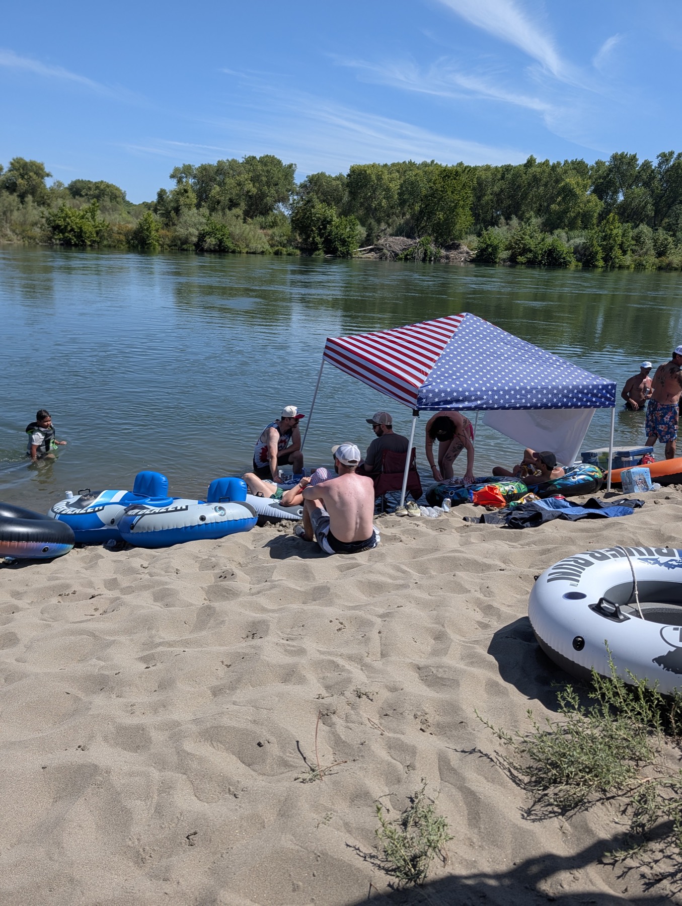 Floaters and tents on the shore of the Sacramento River